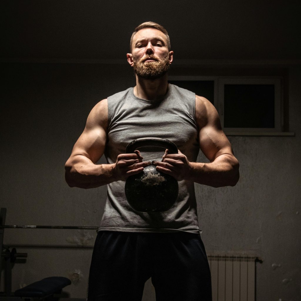Strong man with a beard lifting a kettlebell in a gym, showcasing fitness and strength.
