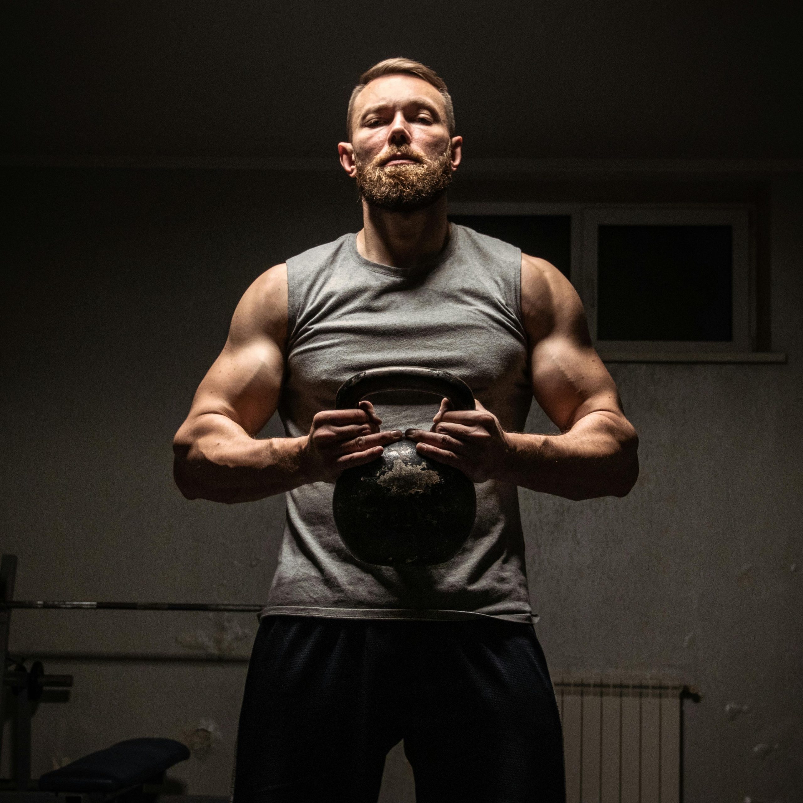 Strong man with a beard lifting a kettlebell in a gym, showcasing fitness and strength.